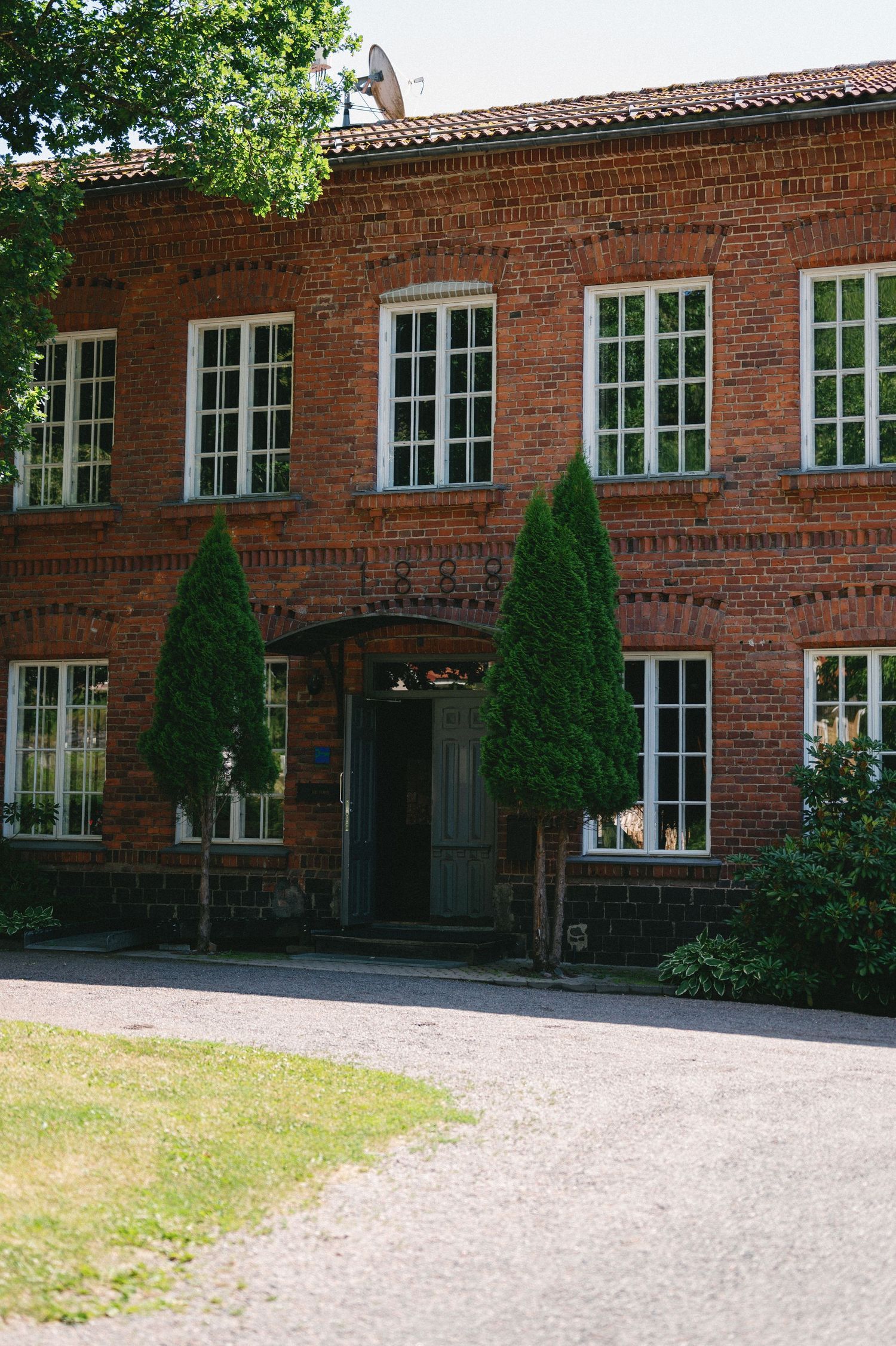 Historic red brick building exterior with white-trimmed windows and decorative topiary trees along the entrance.