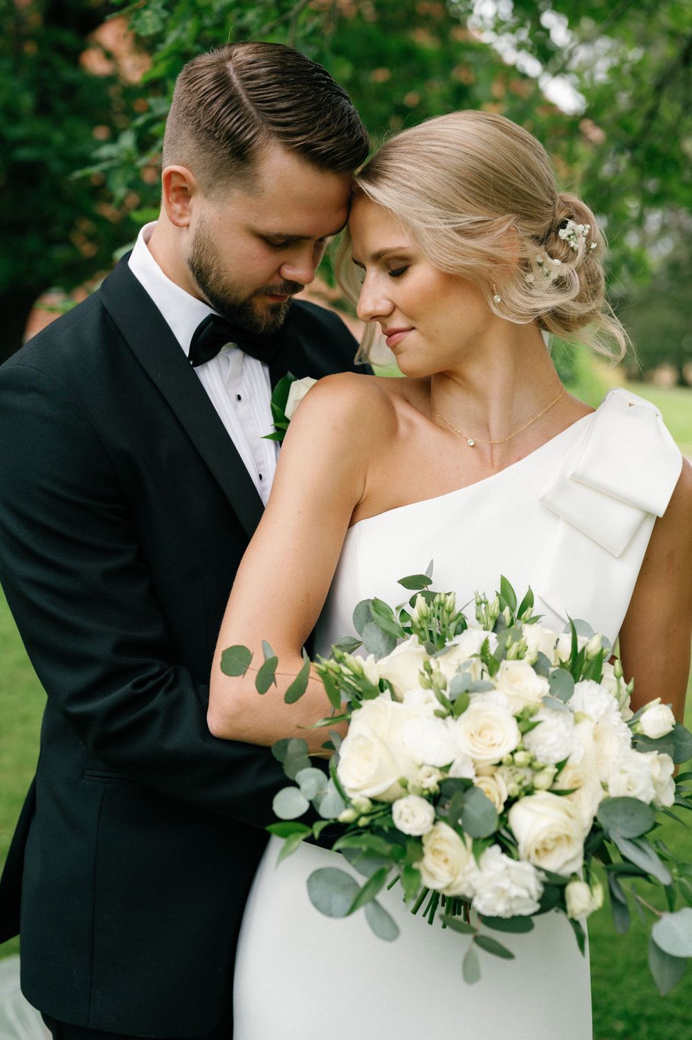 A tender wedding moment photographed with white roses and eucalyptus bouquet details.