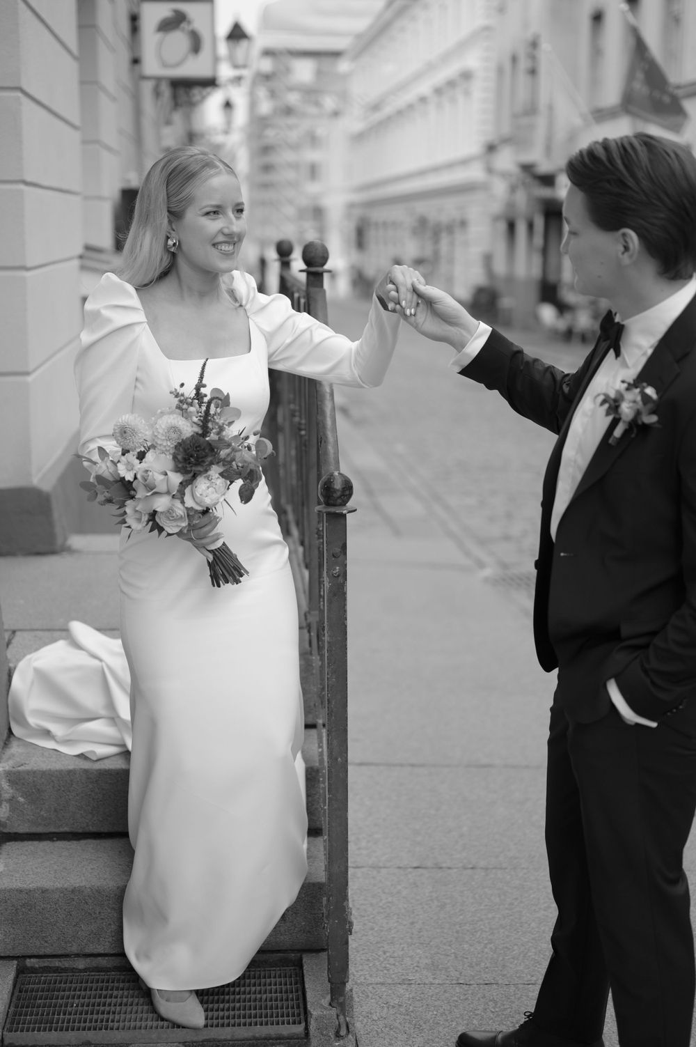 A black and white wedding photo showing a playful moment on urban steps.