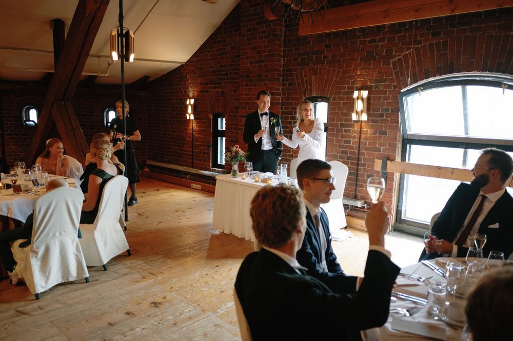 A reception venue with exposed brick walls, large windows, and guests seated at round tables.