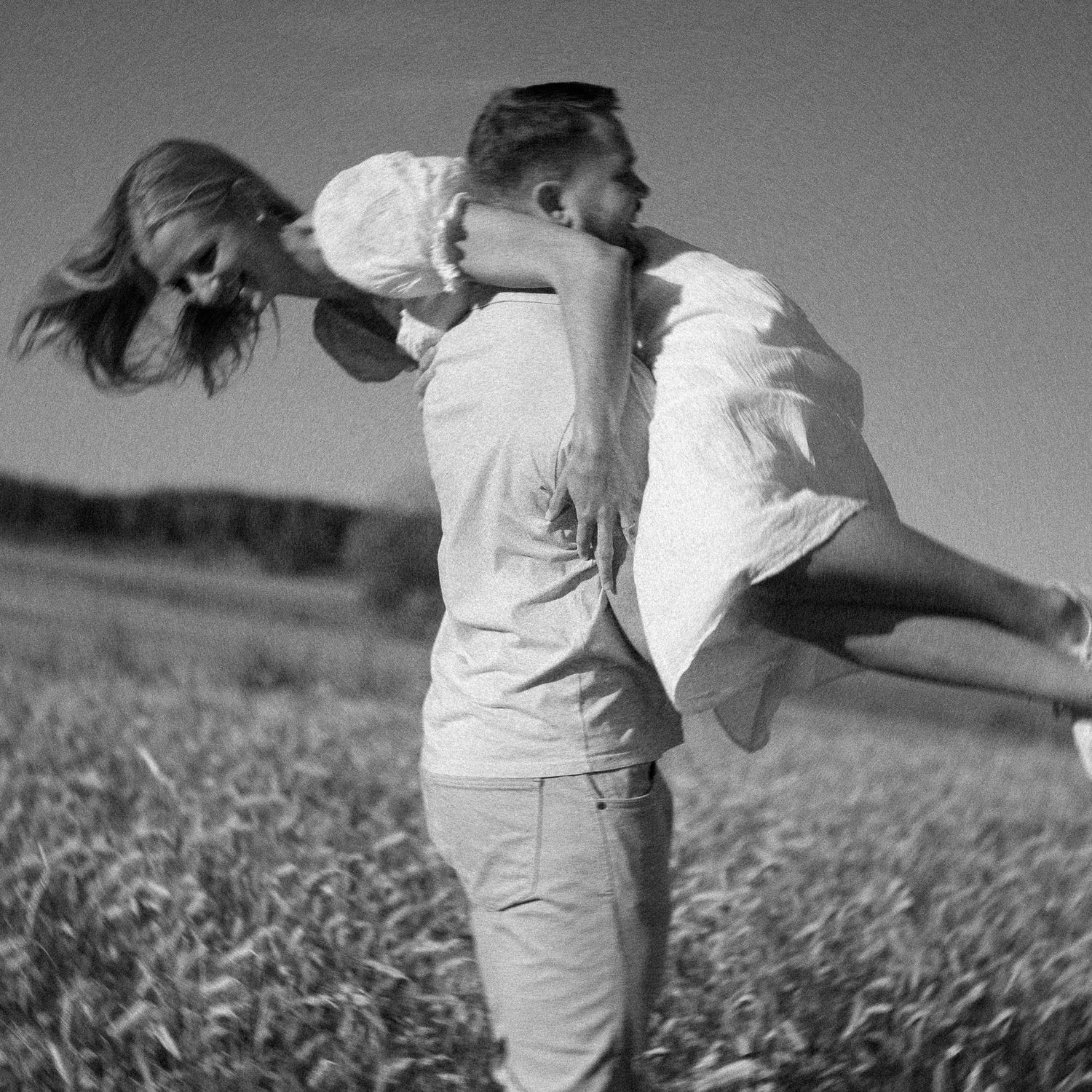 Two people dancing playfully together in a sunny wheat field.