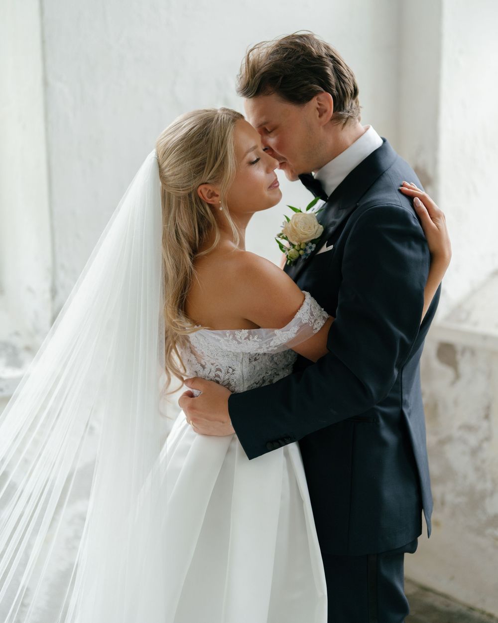 A tender wedding moment with the bride in a lace off-shoulder gown embracing her groom.