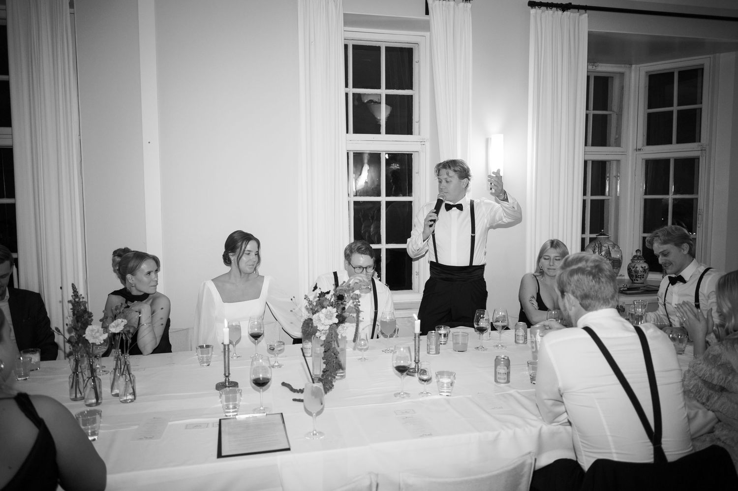 A panoramic black and white view of people seated at tables in an elegant dining room for a formal event.