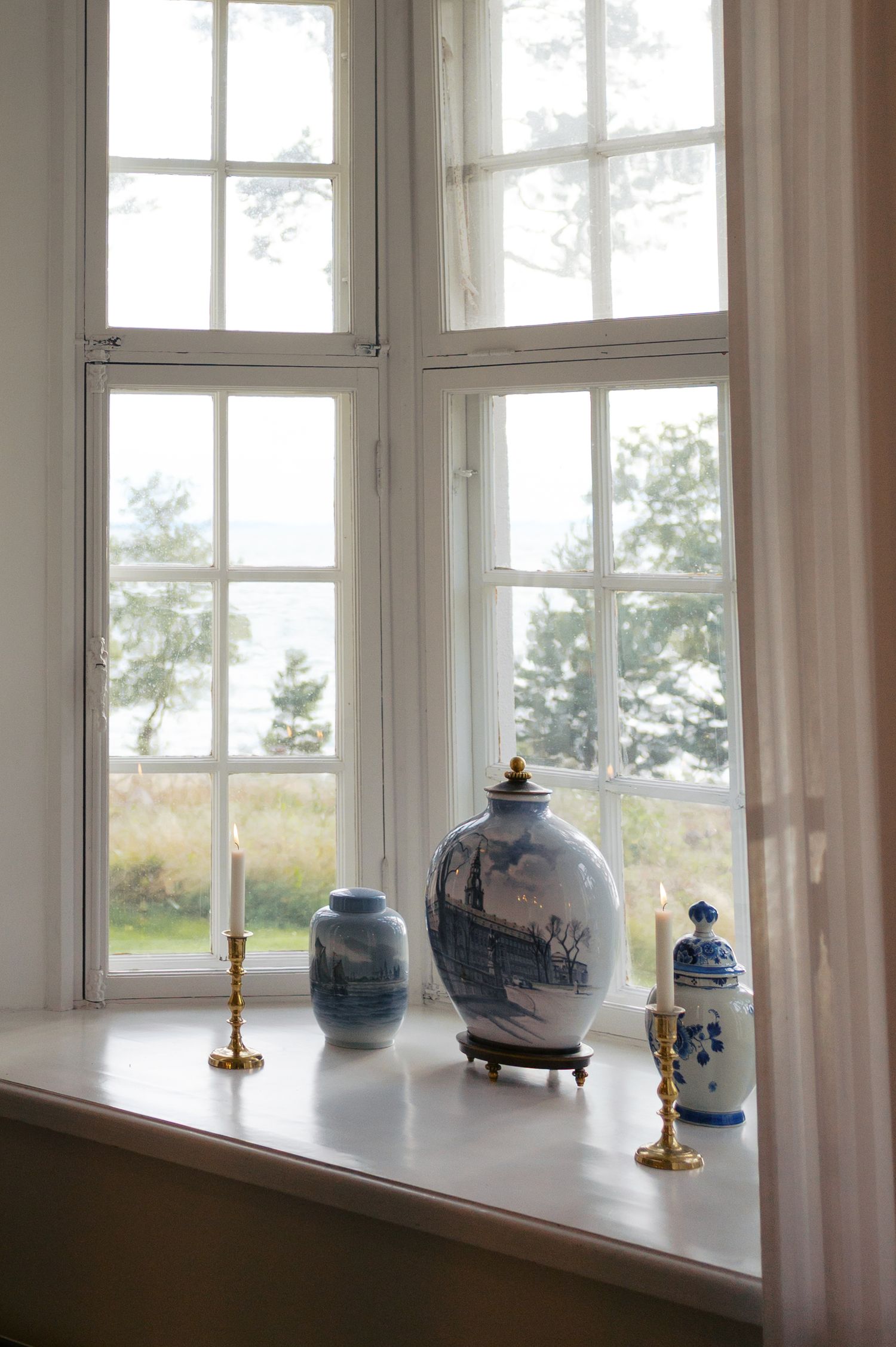 Blue and white ceramic vases and jars displayed along a bright sunlit windowsill in a traditional interior setting.