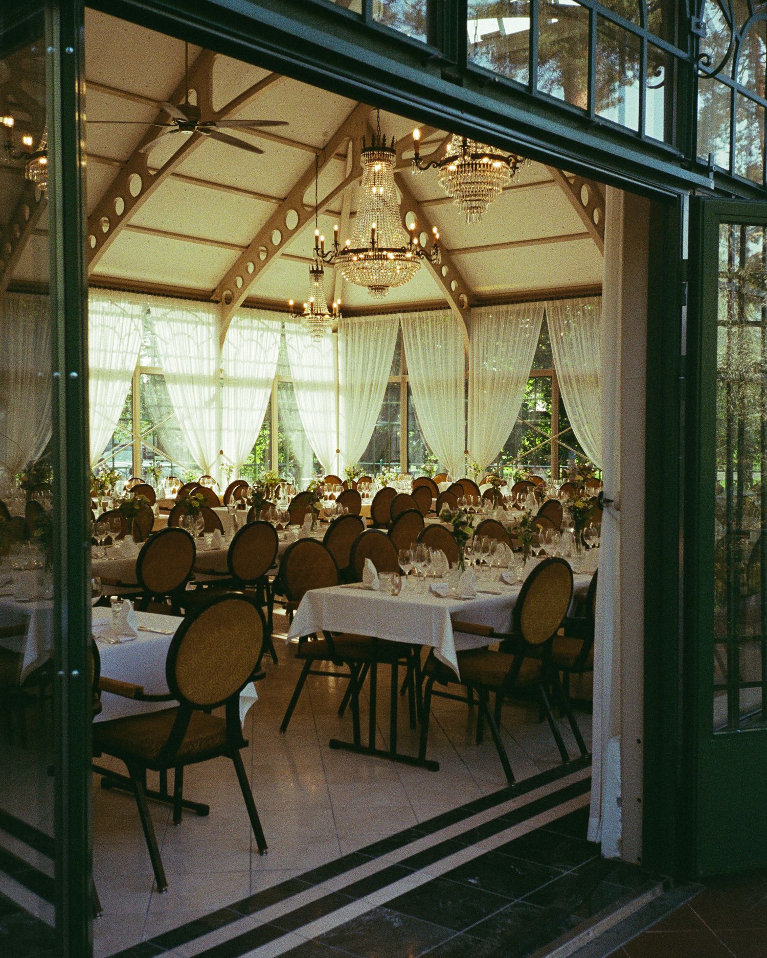 Elegant wedding reception venue with glass walls, chandeliers and formal table settings.