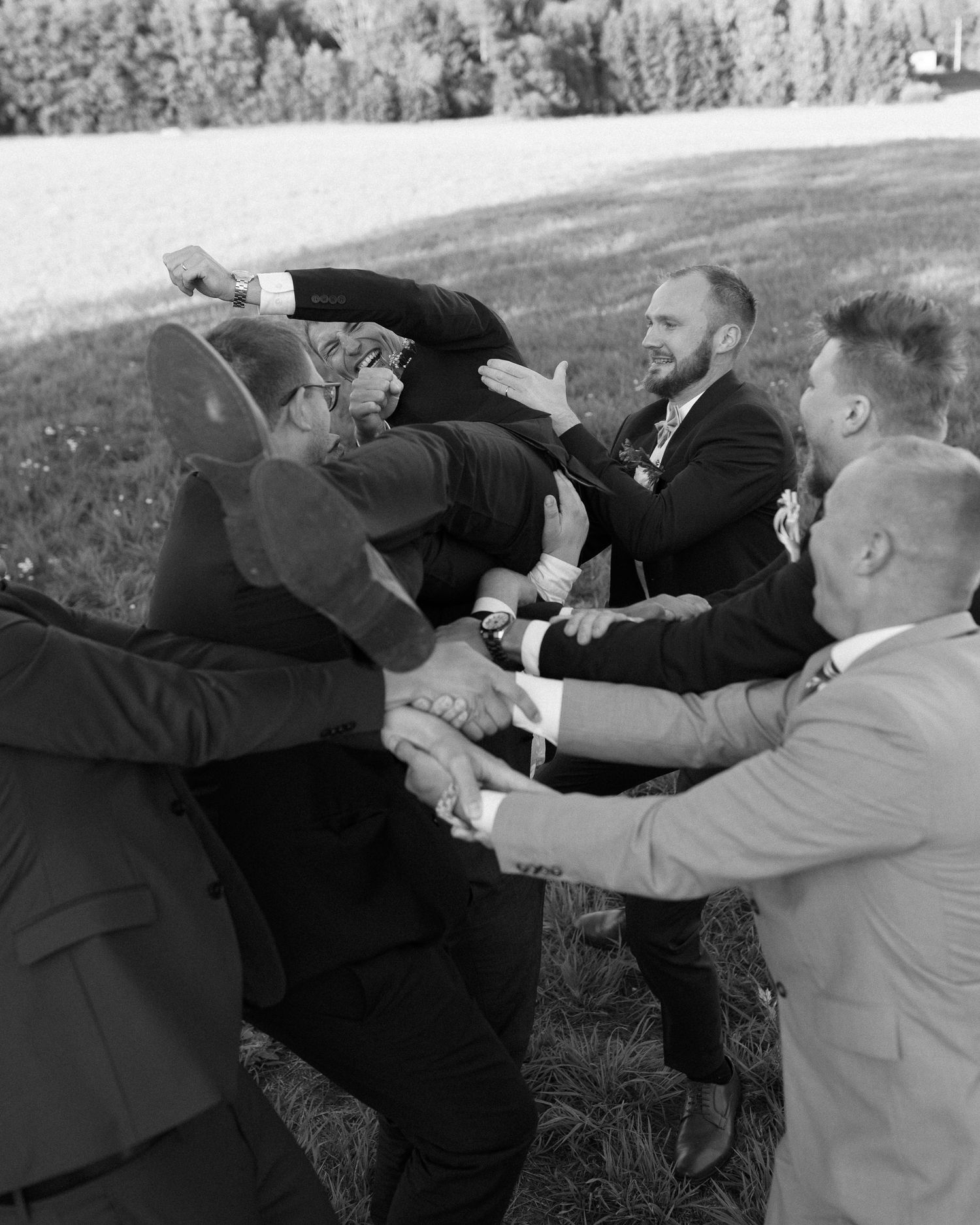 Groomsmen posing playfully in a line outdoors during wedding photography session.