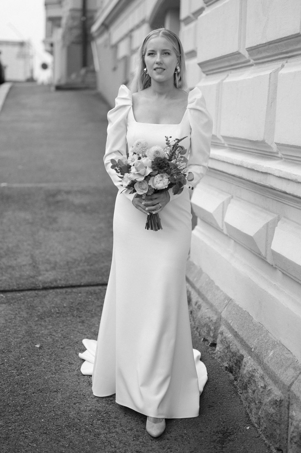 Modern white wedding dress with square neckline and puff sleeves photographed against stone building.
