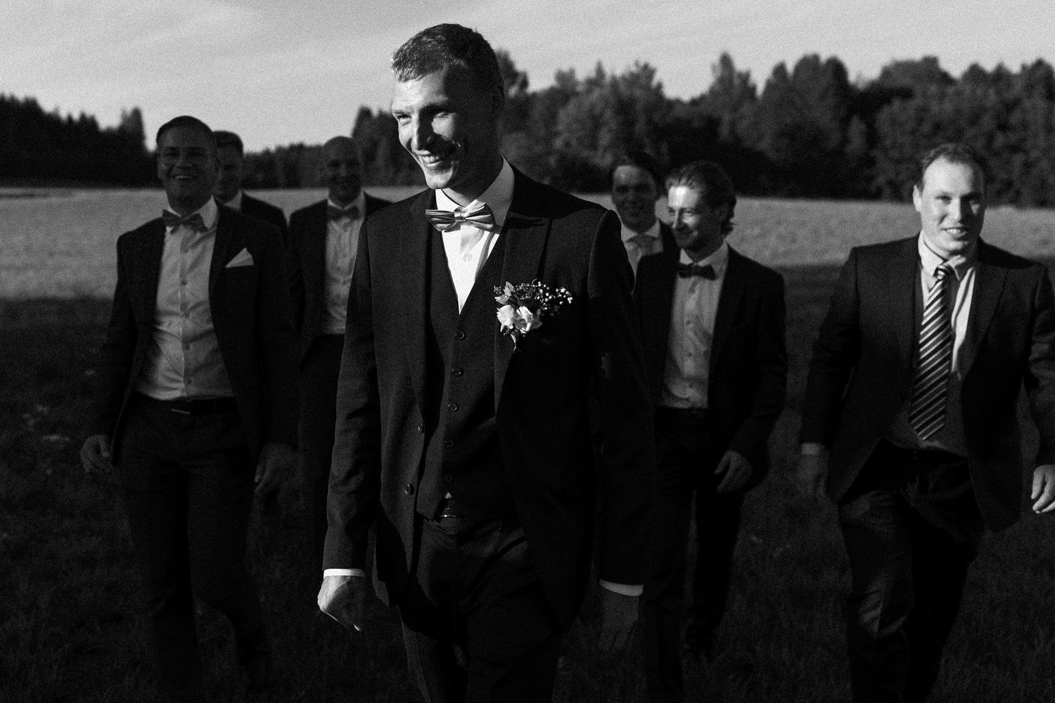 Black and white photo of groomsmen gathered together at an outdoor wedding.