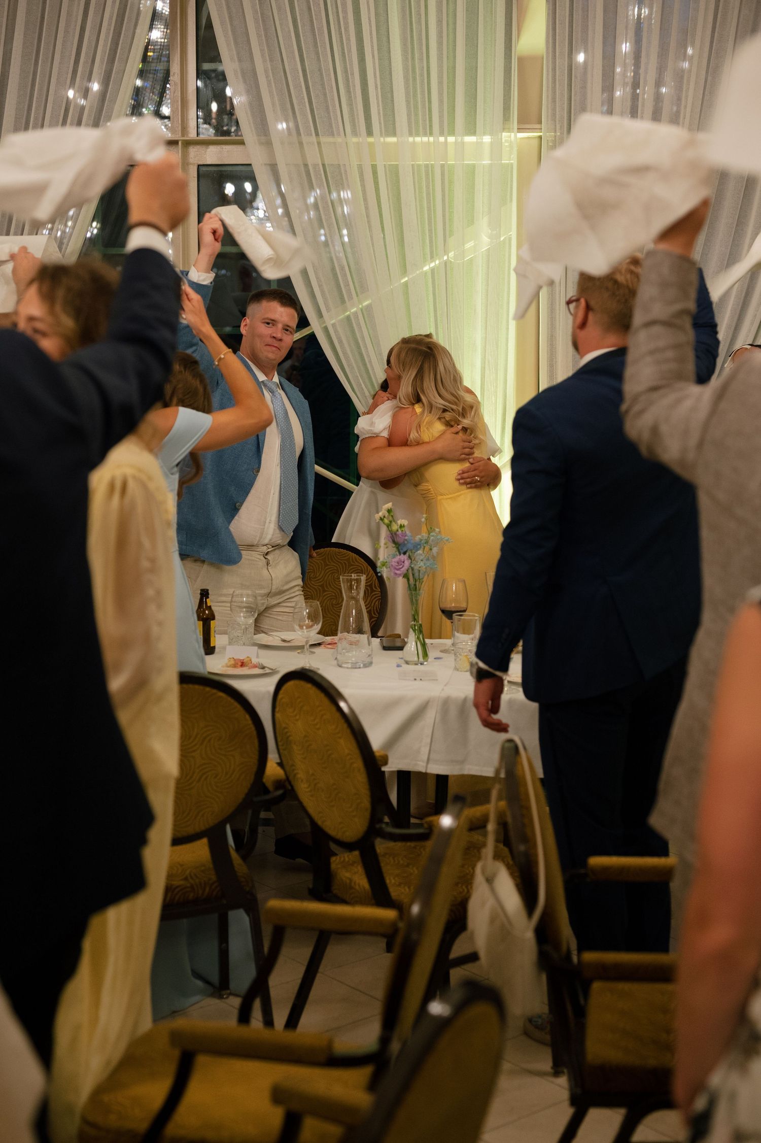 Wedding reception guests dancing and celebrating in a banquet hall with draped curtains.
