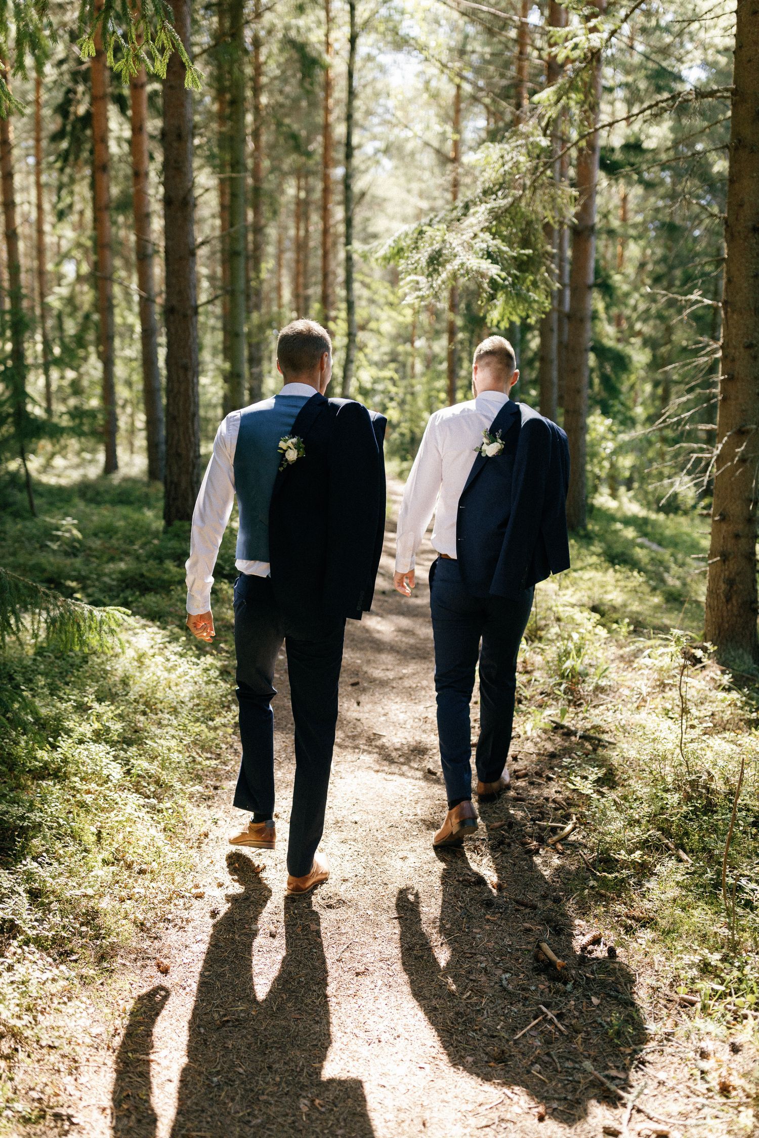 Wedding couple walks hand in hand down a forest path casting long shadows.