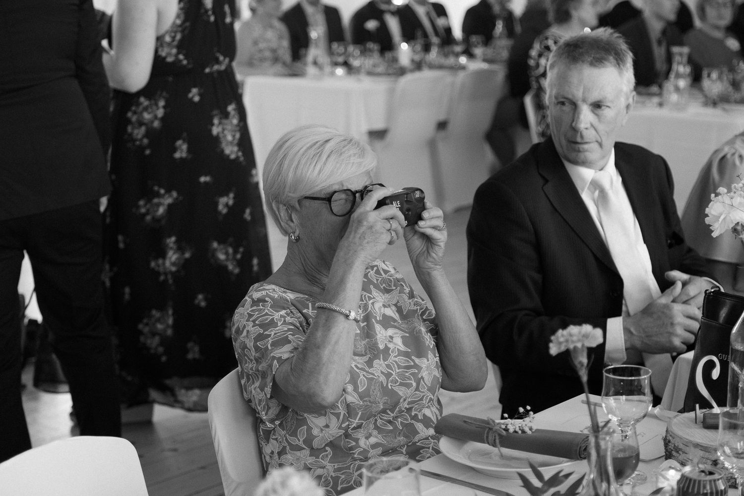 Black and white photo of wedding guests dining at reception tables.