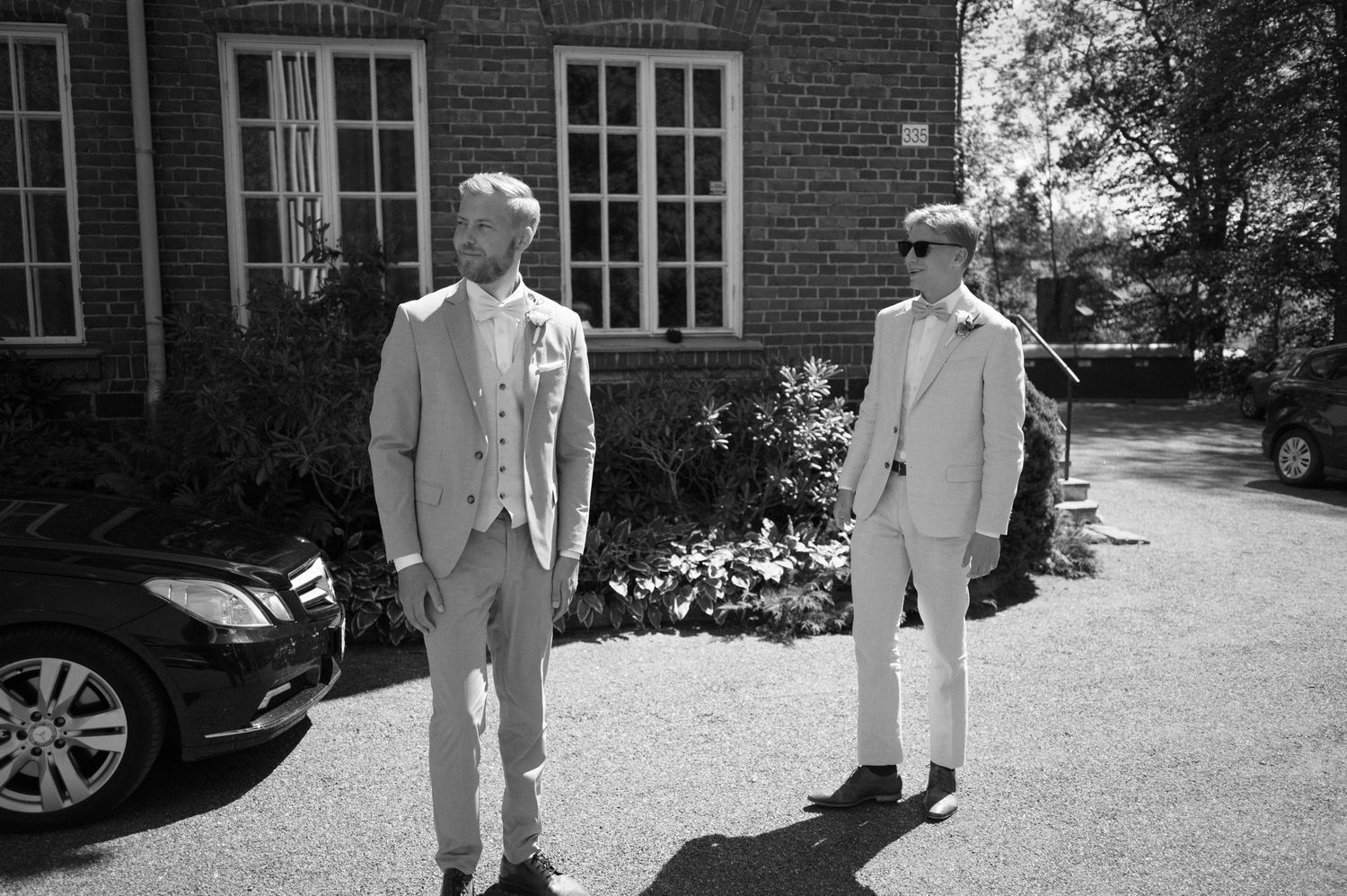 Black and white photo of wedding party outside brick building with car.