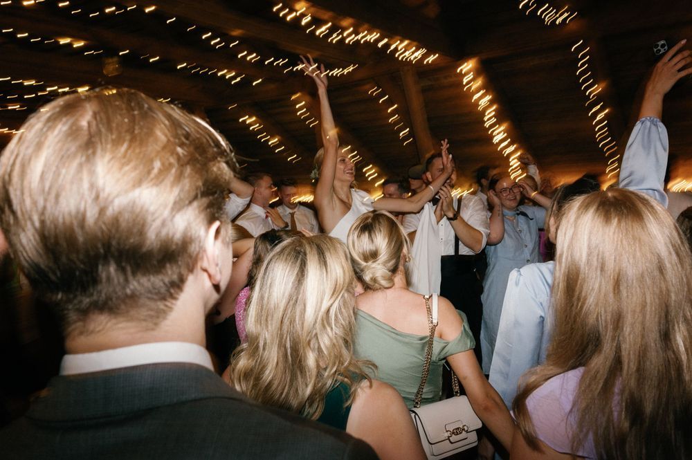 Blurred crowd dancing under warm string lights at indoor reception.