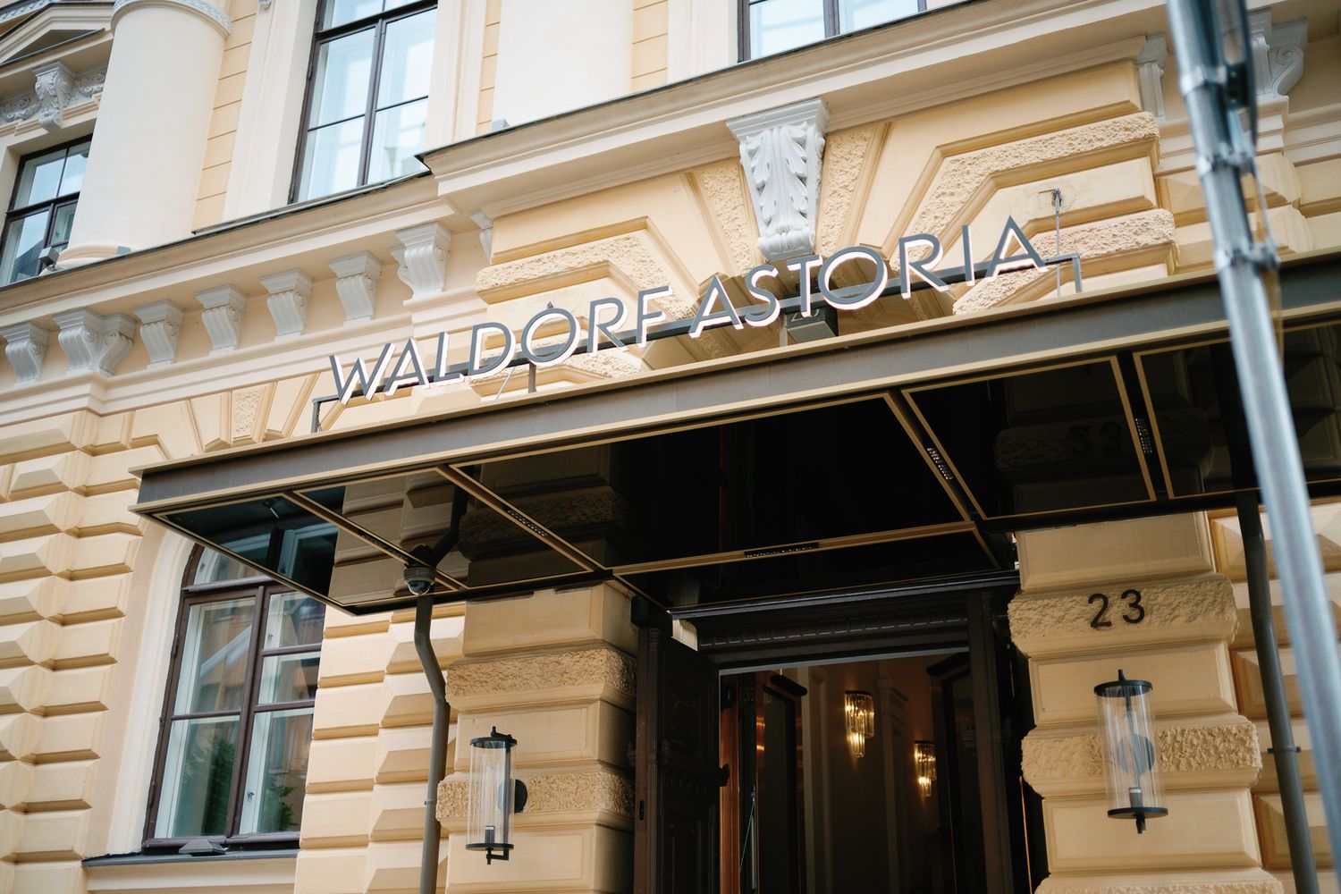 Waldorf Astoria hotel entrance with elegant facade, dark canopy awning, and gold lettering at number 23.