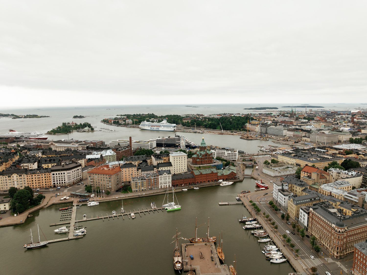 Aerial view of Helsinki harbor with cruise ship, historic buildings, marina, and Baltic Sea islands on overcast day.