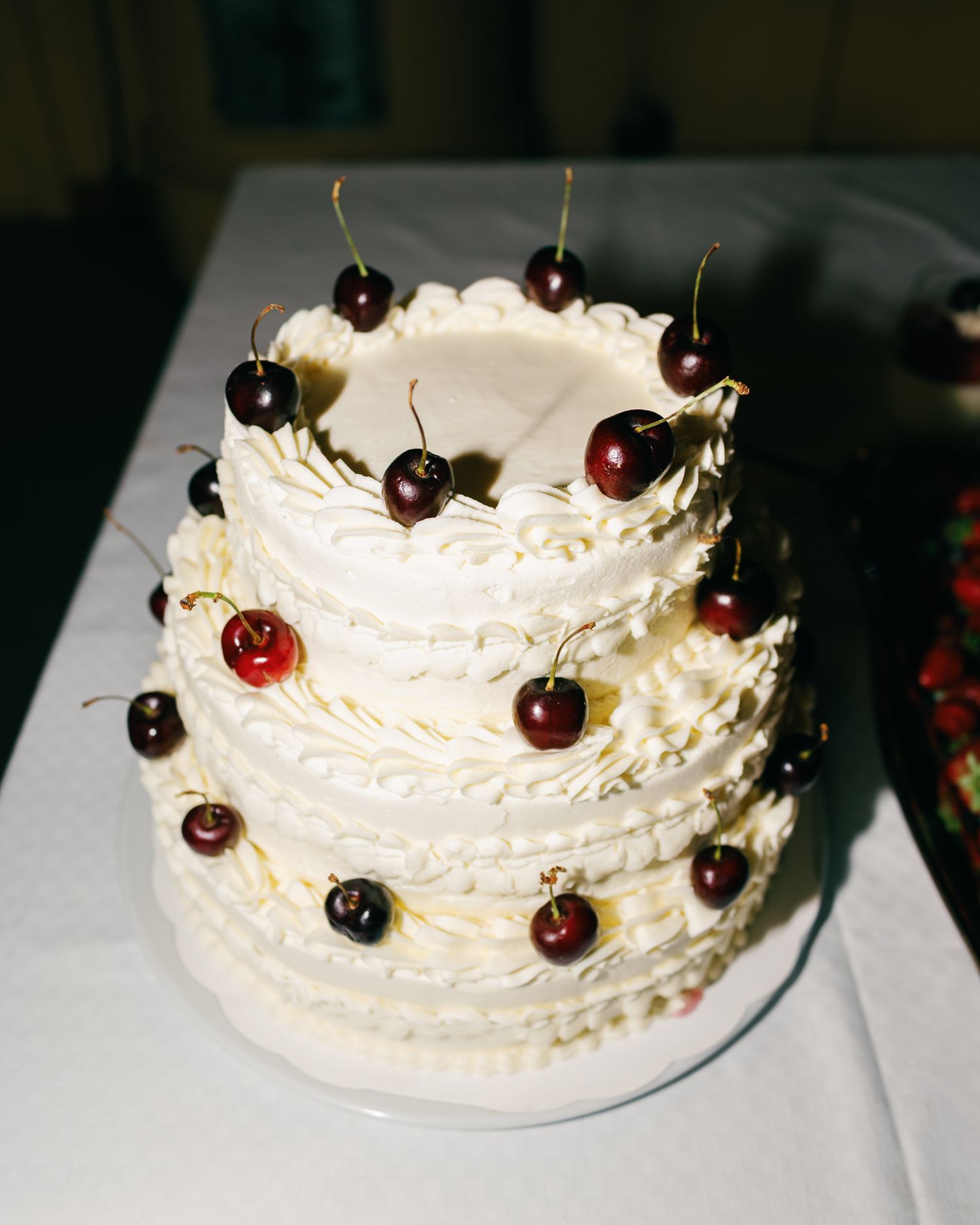 White frosted cake decorated with fresh cherries arranged in a spiral pattern.