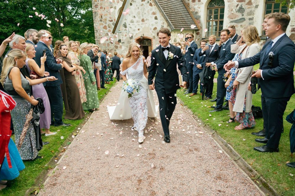Guests line a church pathway throwing confetti during an outdoor wedding celebration.