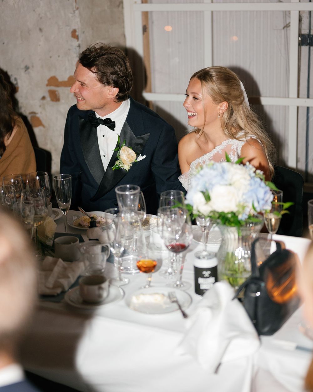 Elegant wedding reception dinner with white tablecloths, glassware, and candlelight in an industrial-chic venue.