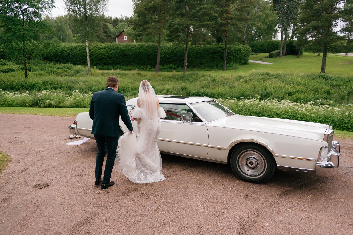 Classic white vintage car parked on a dirt road with trees and greenery in the background.