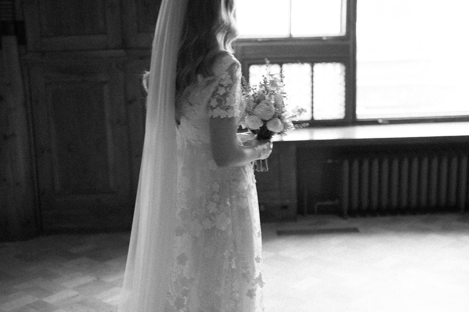 Black and white portrait of a bride holding a bouquet near a window.