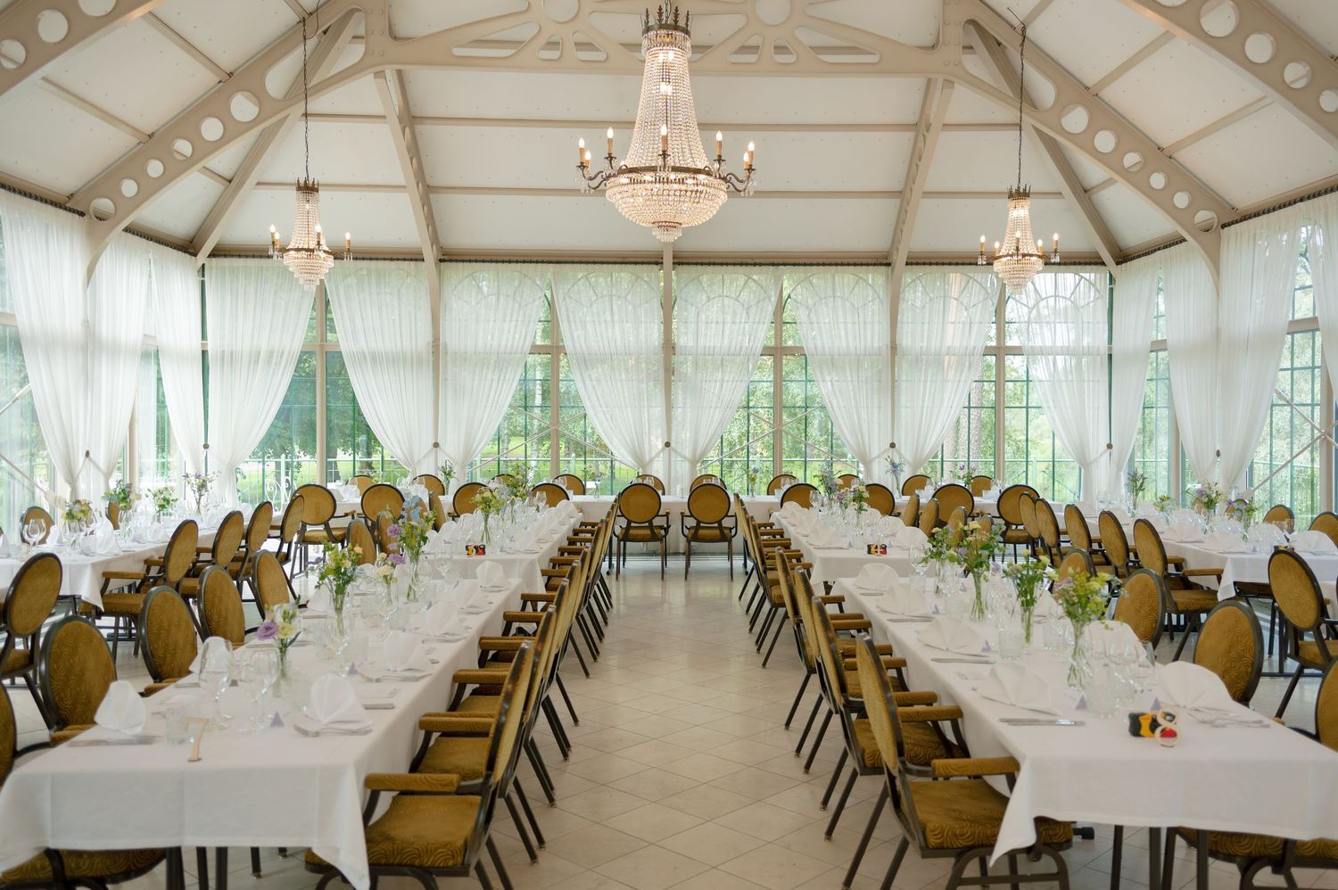 Spacious white tent venue with elegant table settings and gold chairs arranged for a wedding reception.