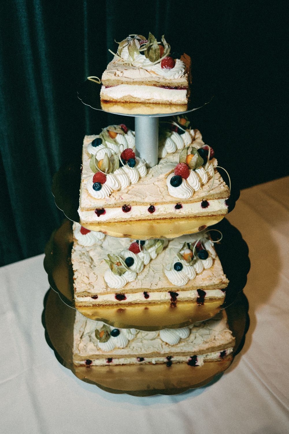 Four-tiered wedding cake decorated with cream, berries and delicate garnishes on a display stand.