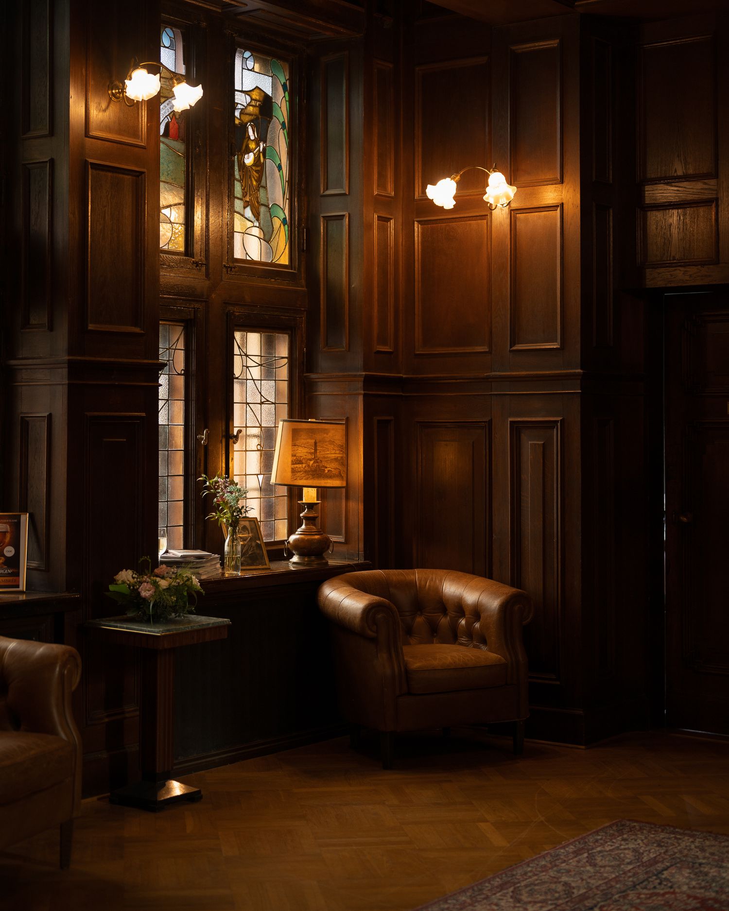 Dark wood-paneled room with warm lighting from vintage wall sconces creating a moody, luxurious atmosphere.