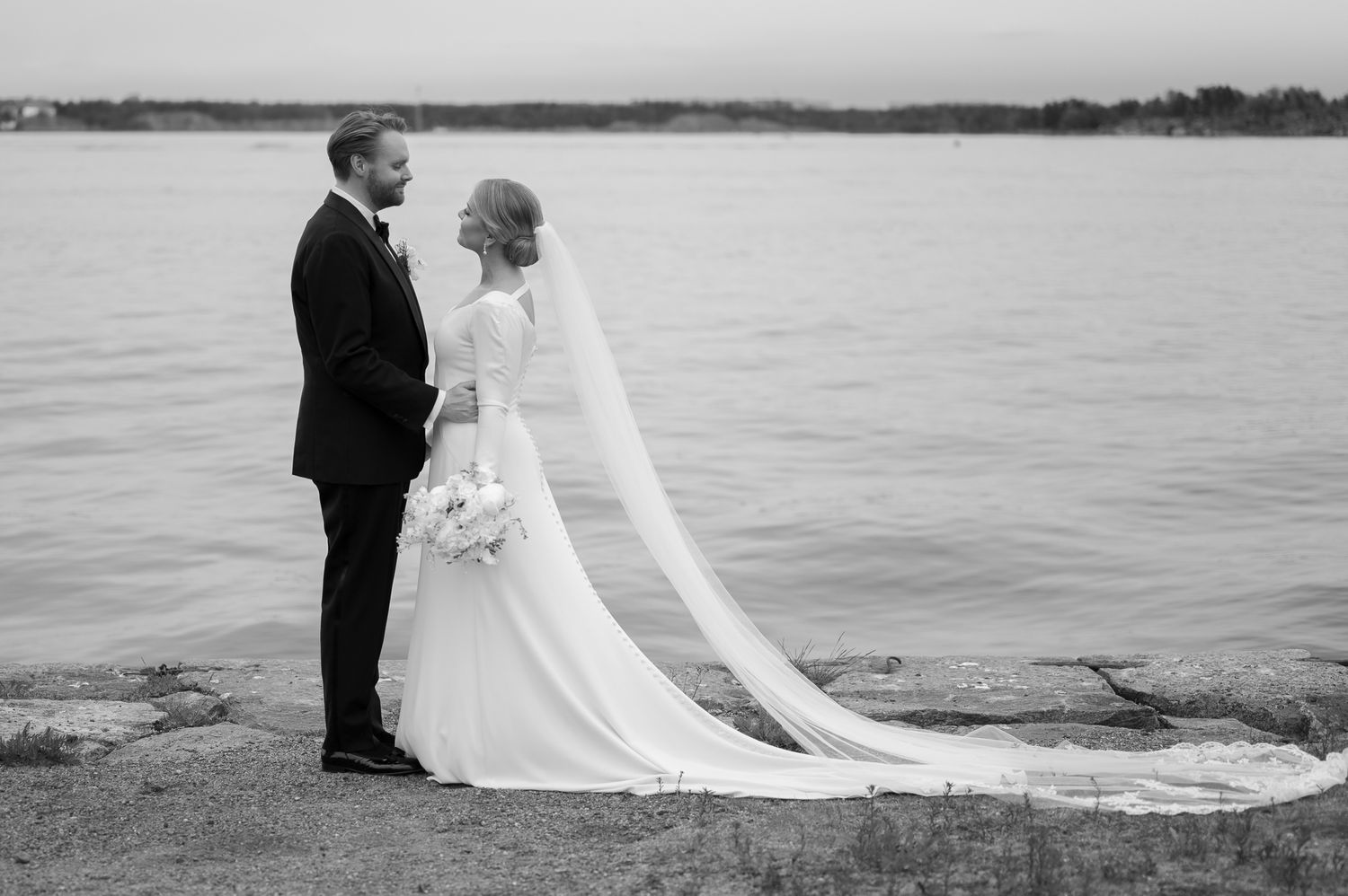 A romantic black and white wedding photo series showing a couple embracing by a serene waterfront.