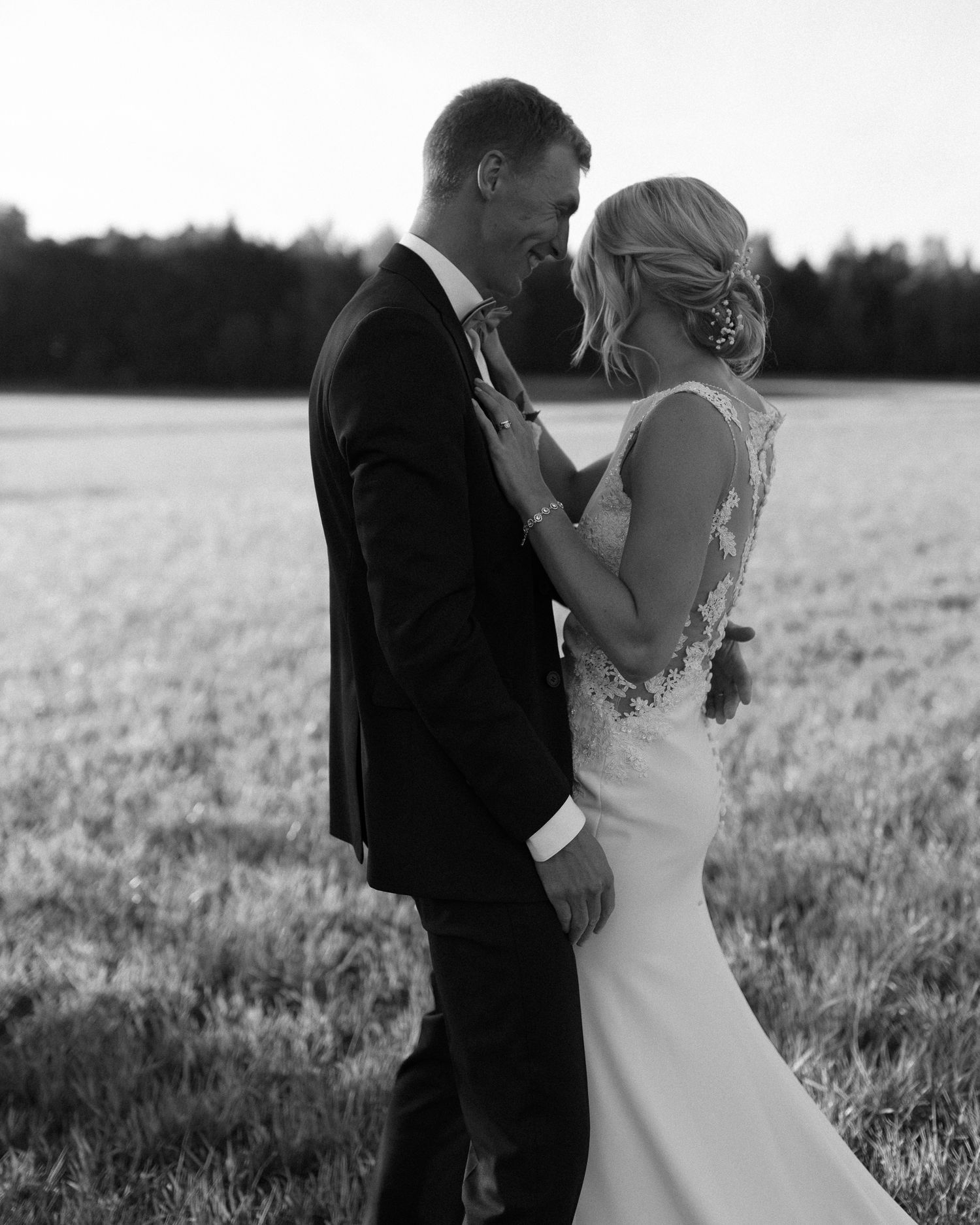 Elegant black and white wedding photo capturing tender moment between bride and groom in field.