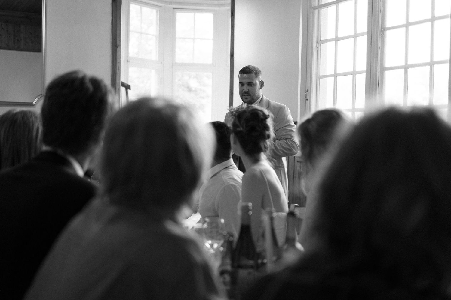 Large windows illuminate an elegant reception hall filled with wedding guests.