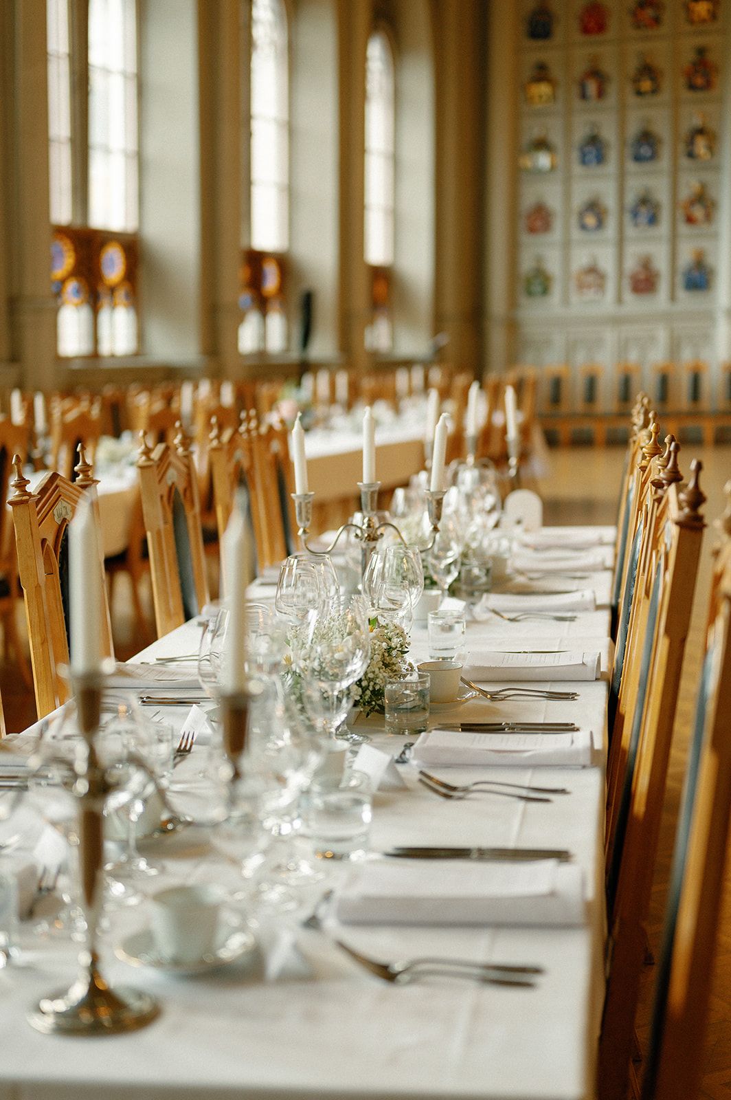 Long formal dining table set with elegant place settings and wooden chairs in a grand hall.