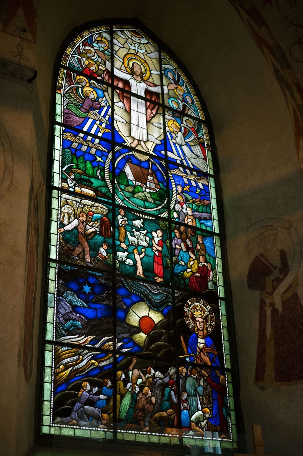 Colorful stained glass church window depicting religious scenes with vibrant blue and gold details.