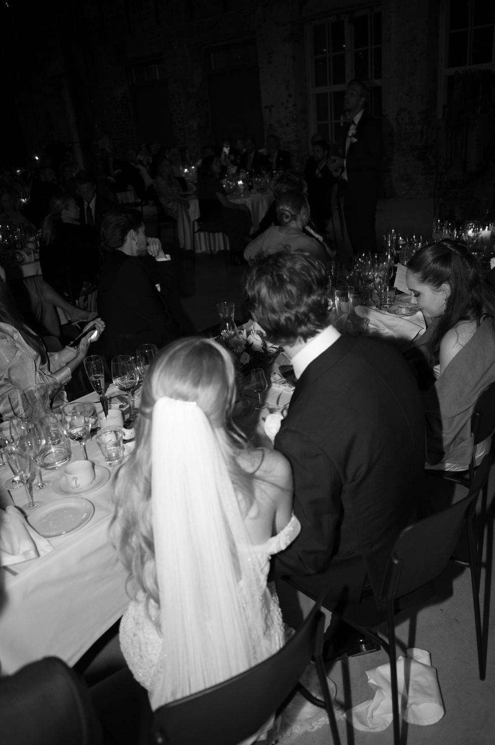 Black and white photo of wedding guests seated at dinner tables during an evening reception.