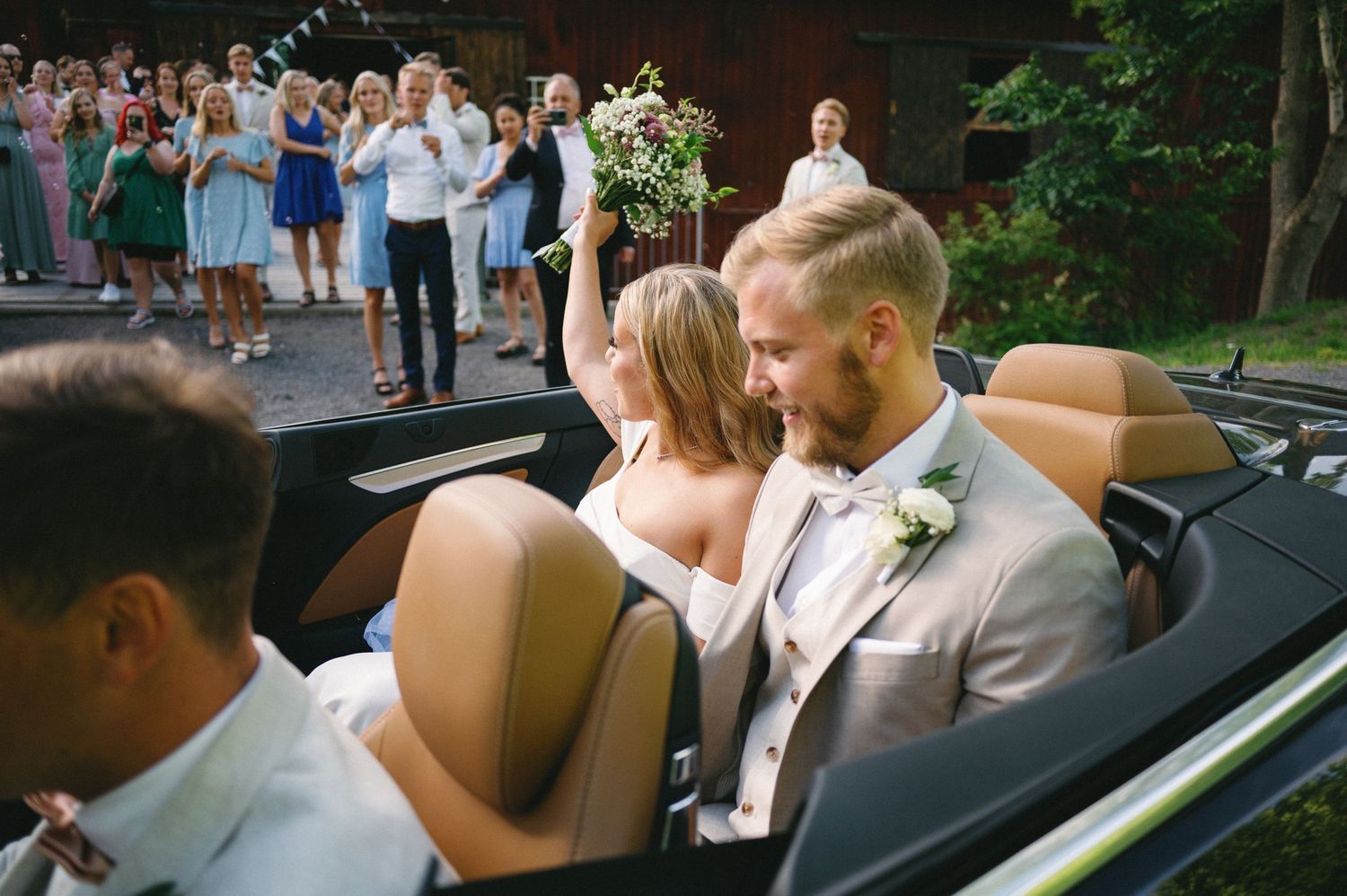 Newlyweds ride in a classic convertible car after their wedding ceremony.