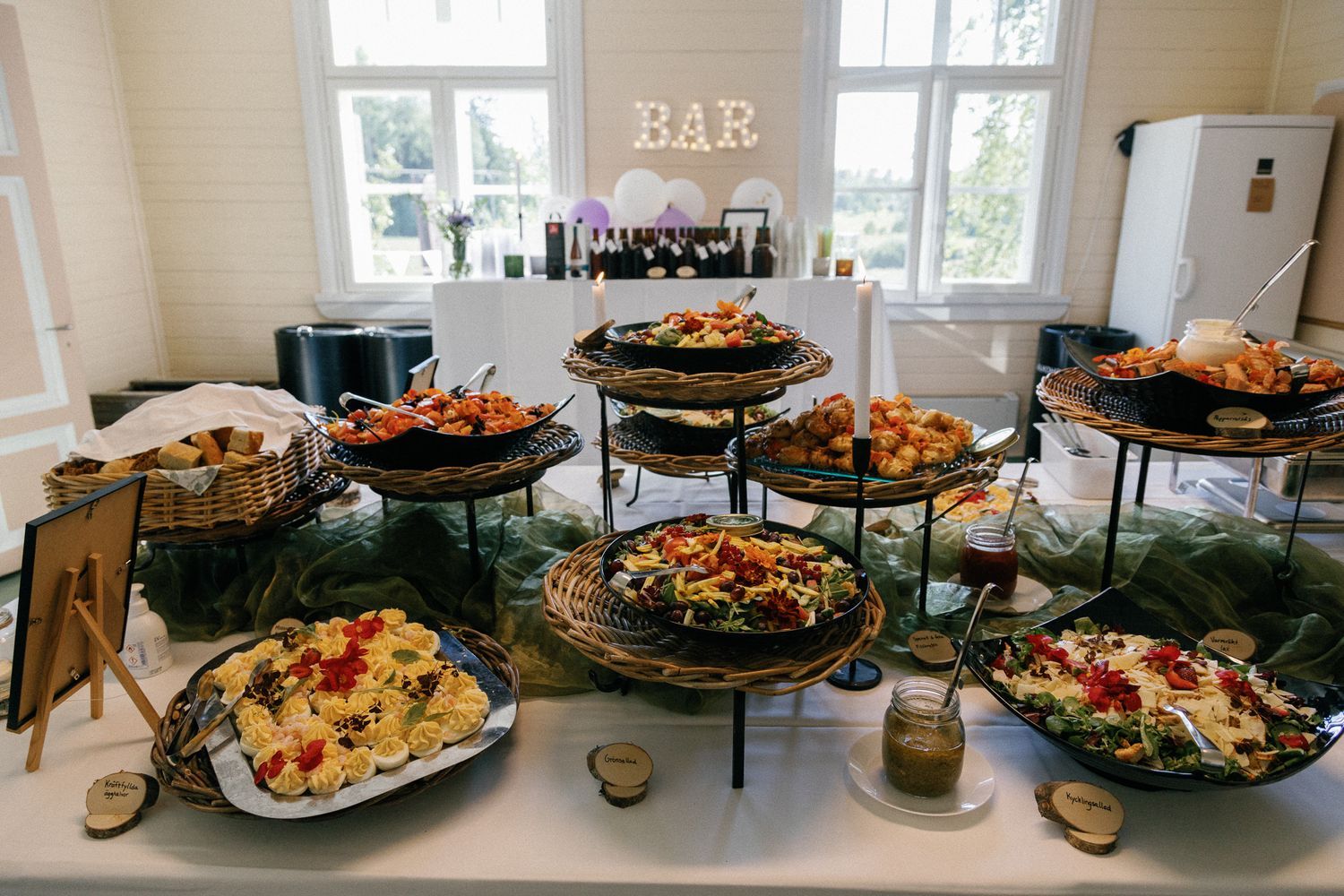 Catering buffet display with multiple tiers of appetizers and fresh food near bar area.