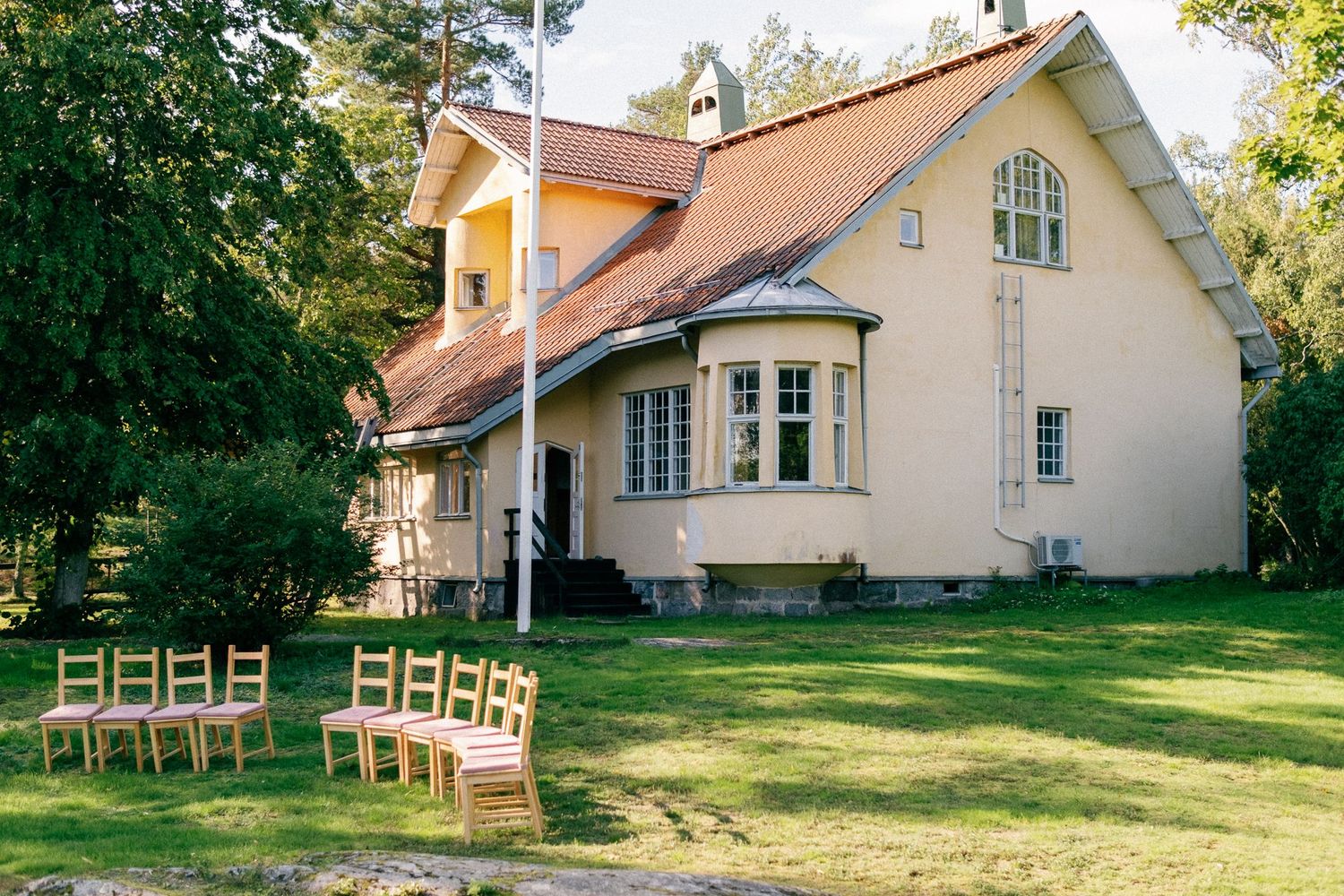 Charming pale yellow house with wooden chairs arranged on the lawn.