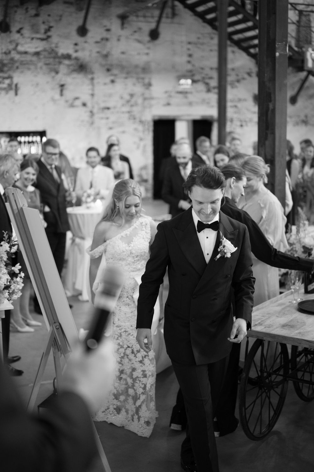 Black and white photos of wedding guests mingling and dancing in a rustic brick venue.