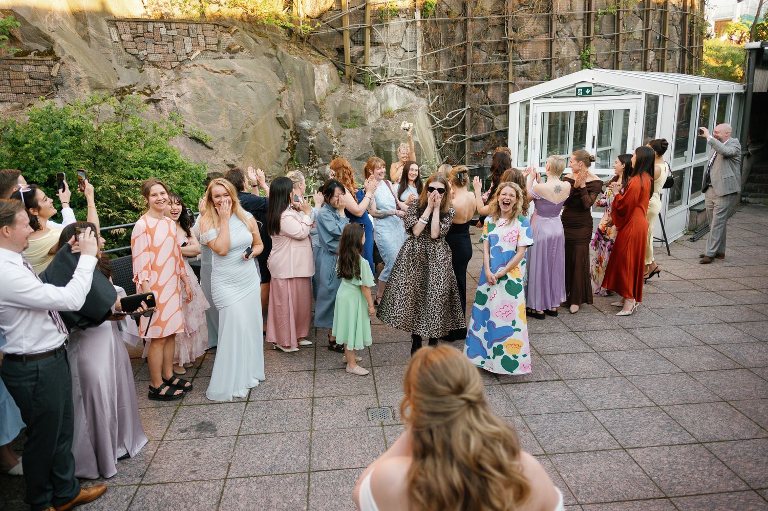 Guests raise their hands and celebrate at an outdoor wedding reception on a stone patio with lush greenery.