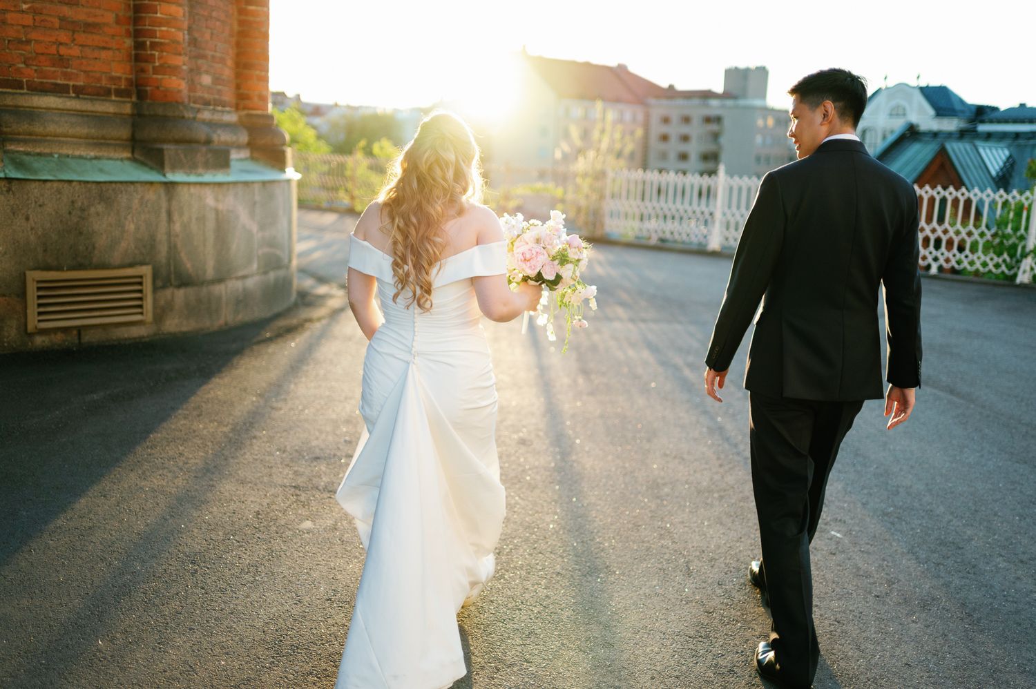 Bride and groom walking together in golden sunset light, bride holding white bouquet in elegant off-shoulder gown.