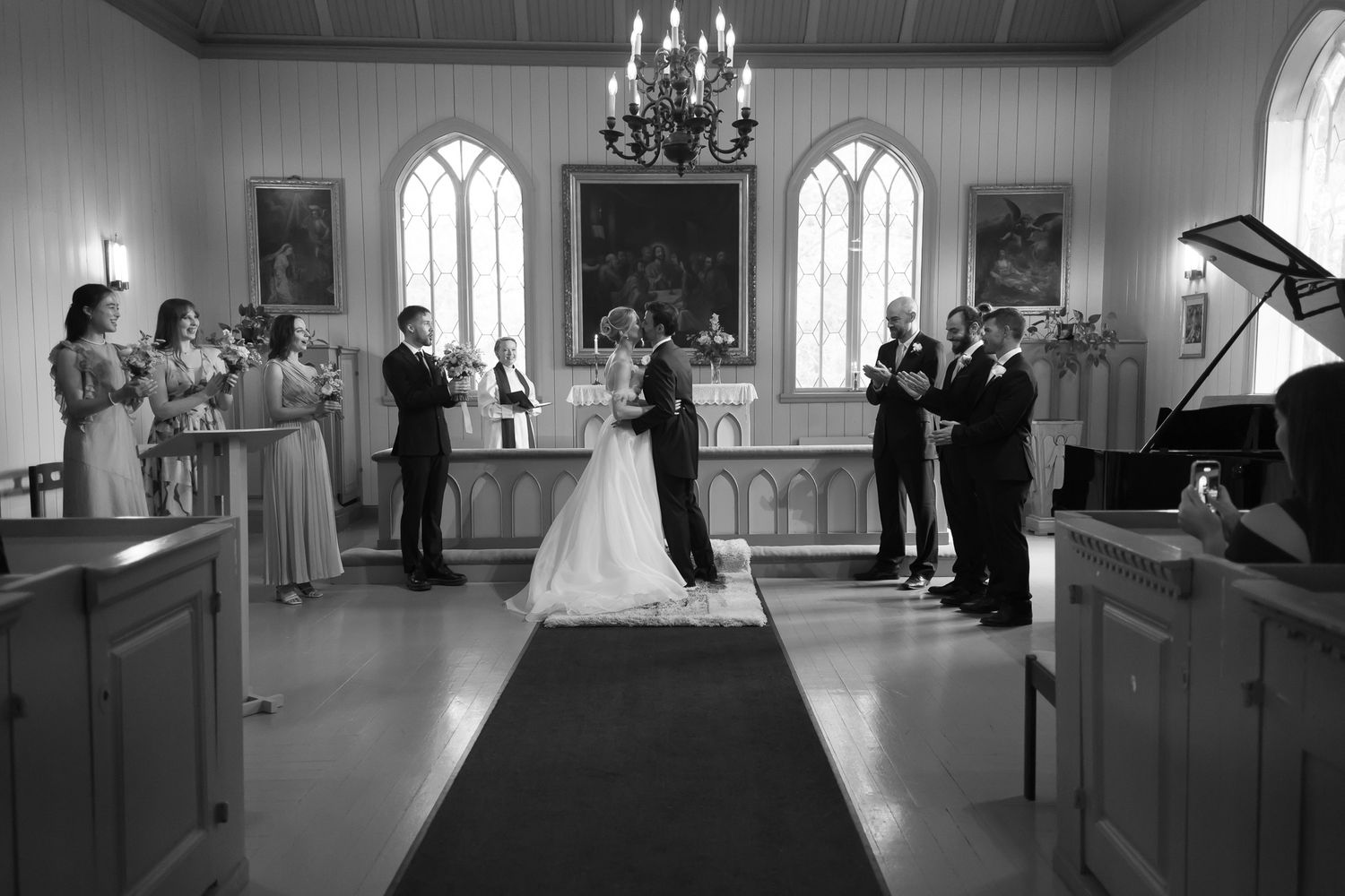 Black and white photo of a wedding ceremony inside a traditional church with bride, groom, and guests gathered at the altar.