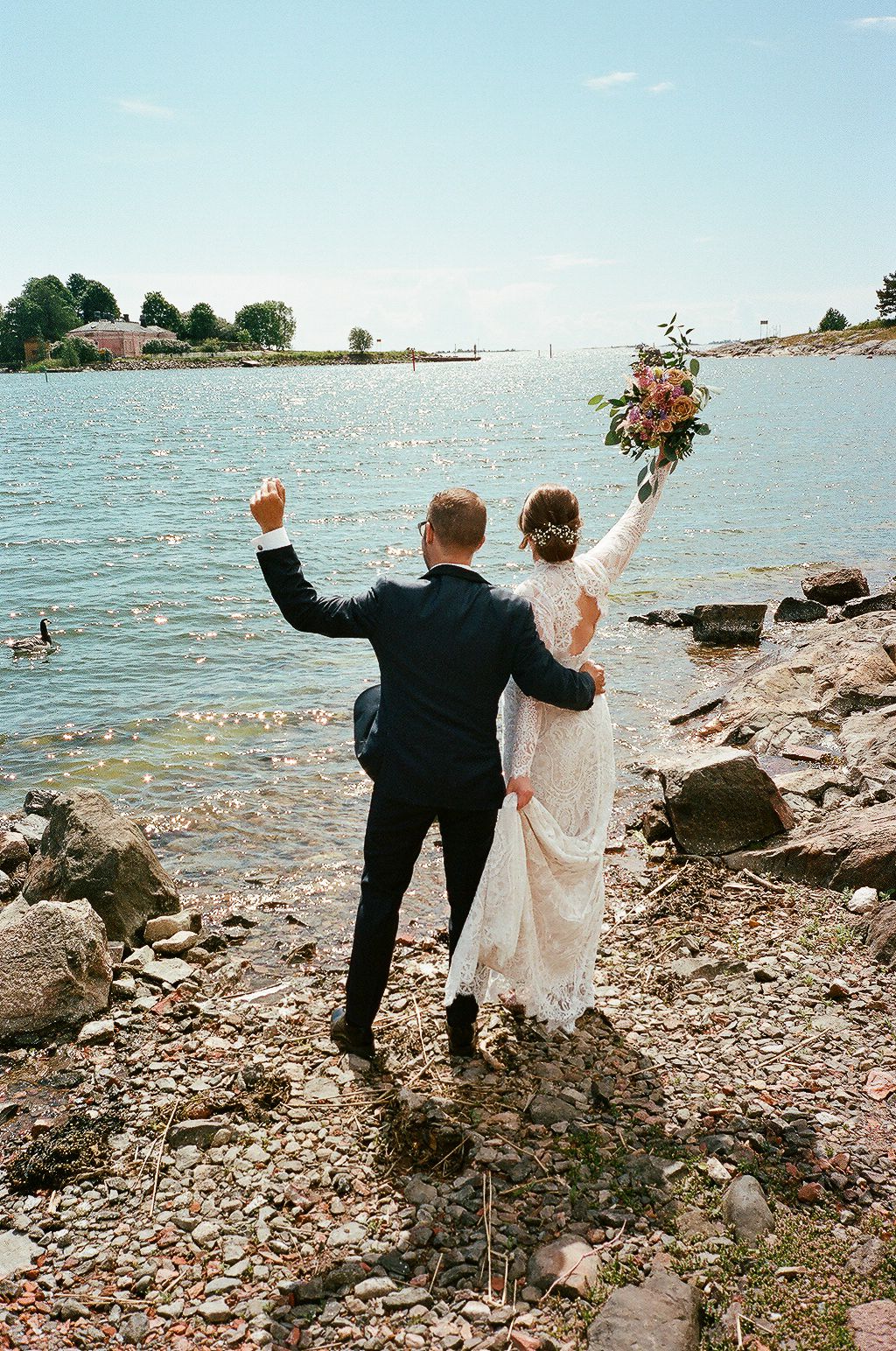 A couple celebrates on a rocky beach shoreline with arms raised in joy.