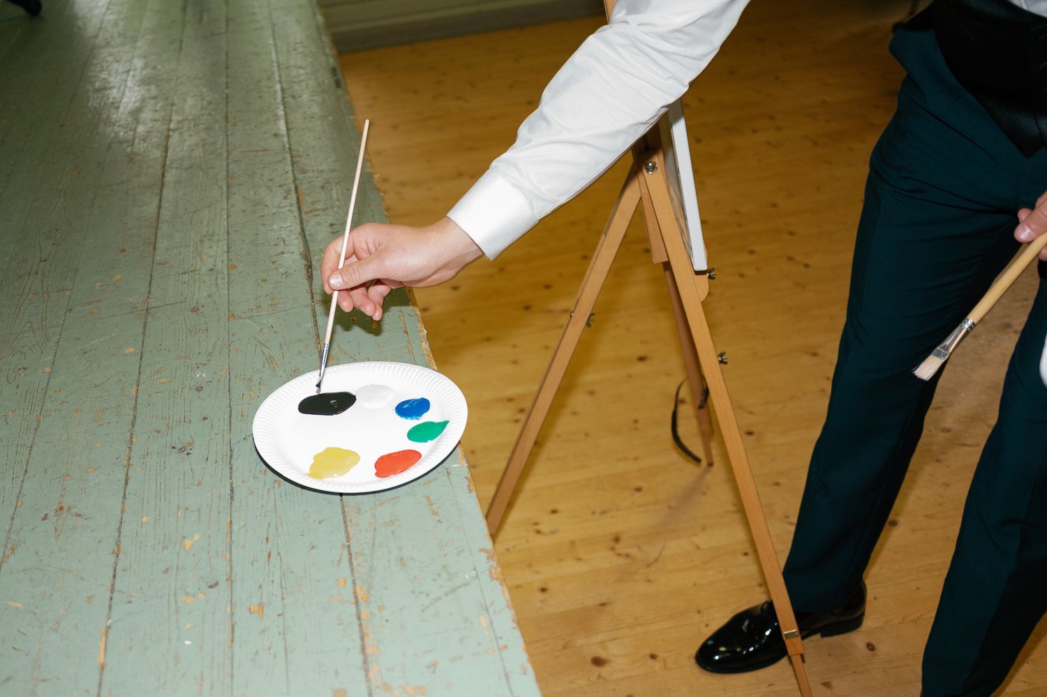 Artist's hand holding paint palette against wooden floor during event.