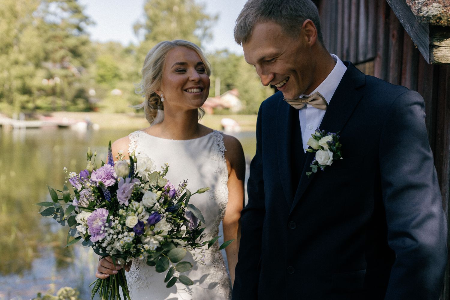 Newlyweds pose for photos near a lake with beautiful floral bouquet and natural scenery.