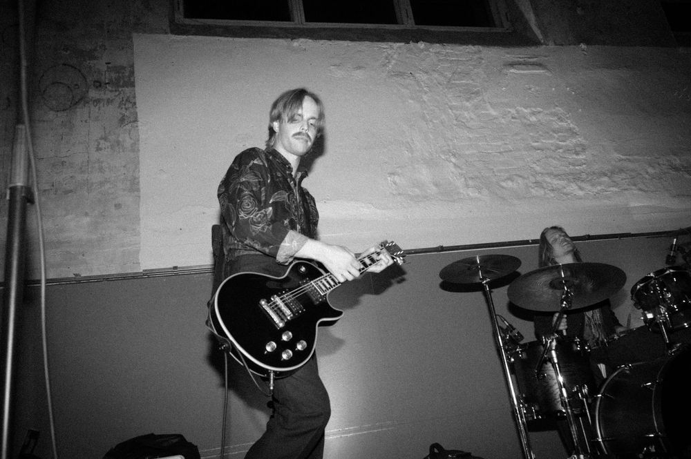Musicians performing on stage with guitars and drums in a monochrome setting.