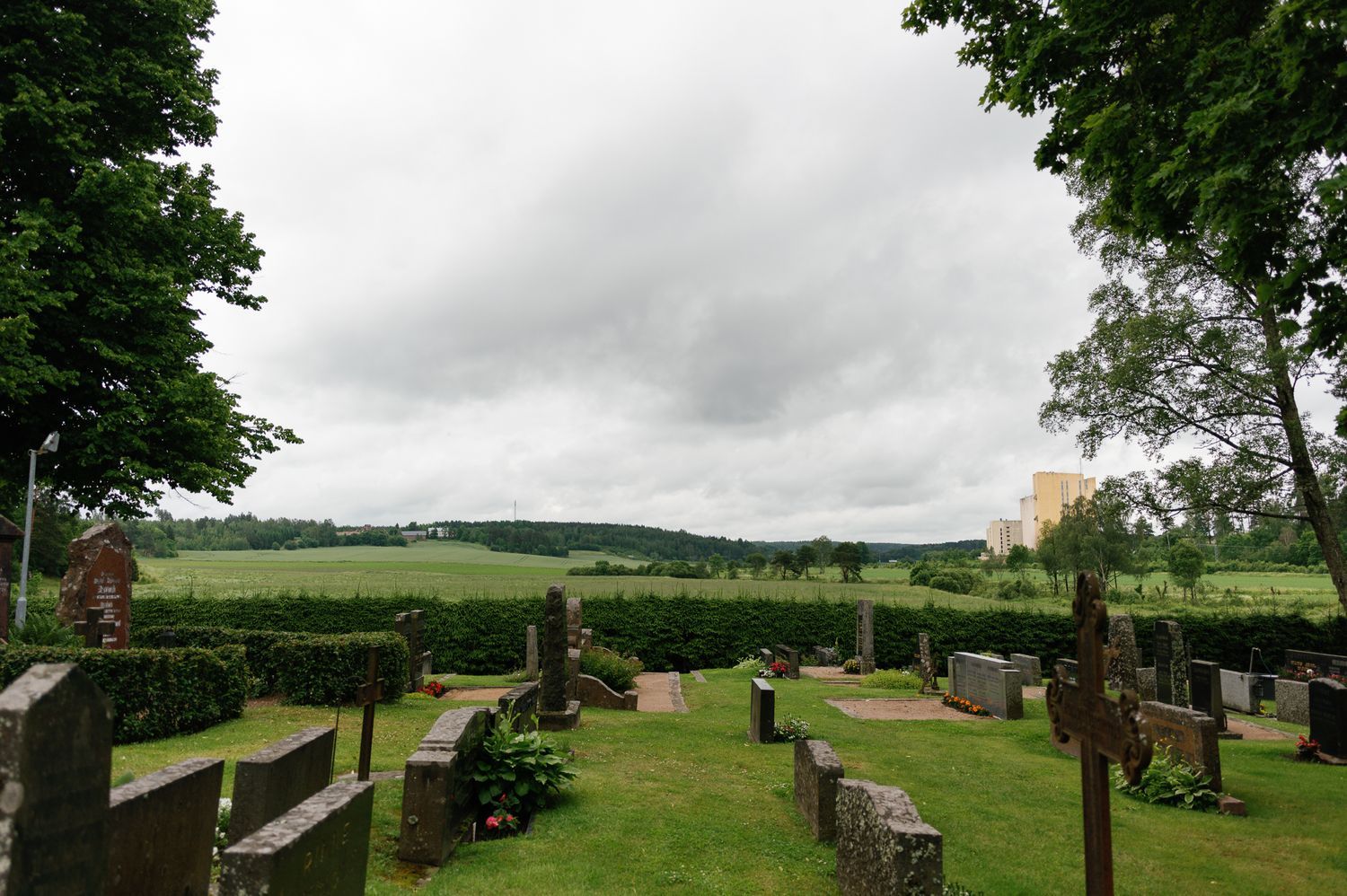 Rural cemetery with old gravestones surrounded by green fields and trees.