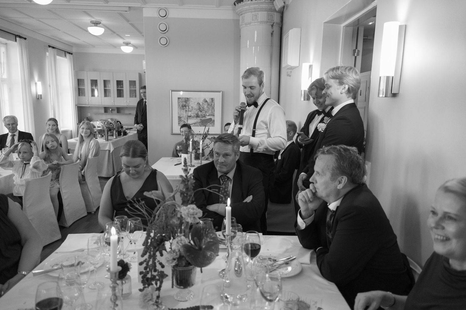 A black and white photograph of people gathered at an elegant dining table in what appears to be a formal restaurant setting.