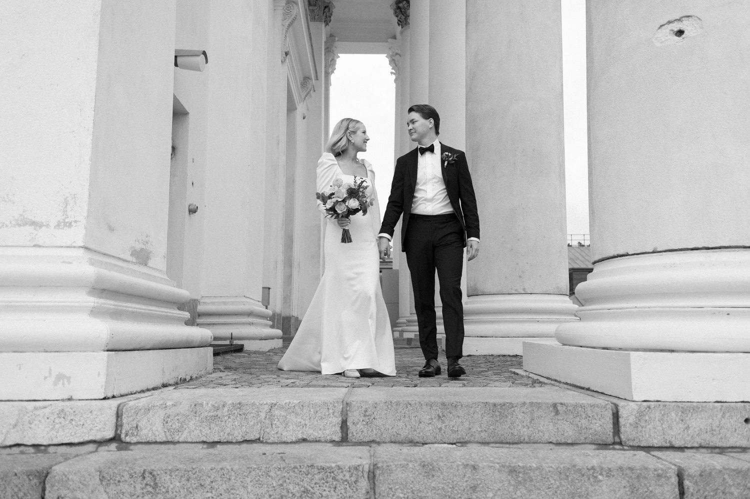 Classic black and white photo of newlyweds standing between white columns.
