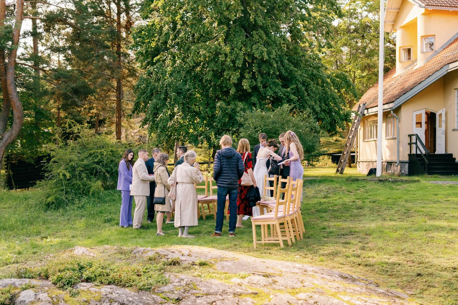 Wedding celebration in a lush green garden with guests gathered near a yellow house.