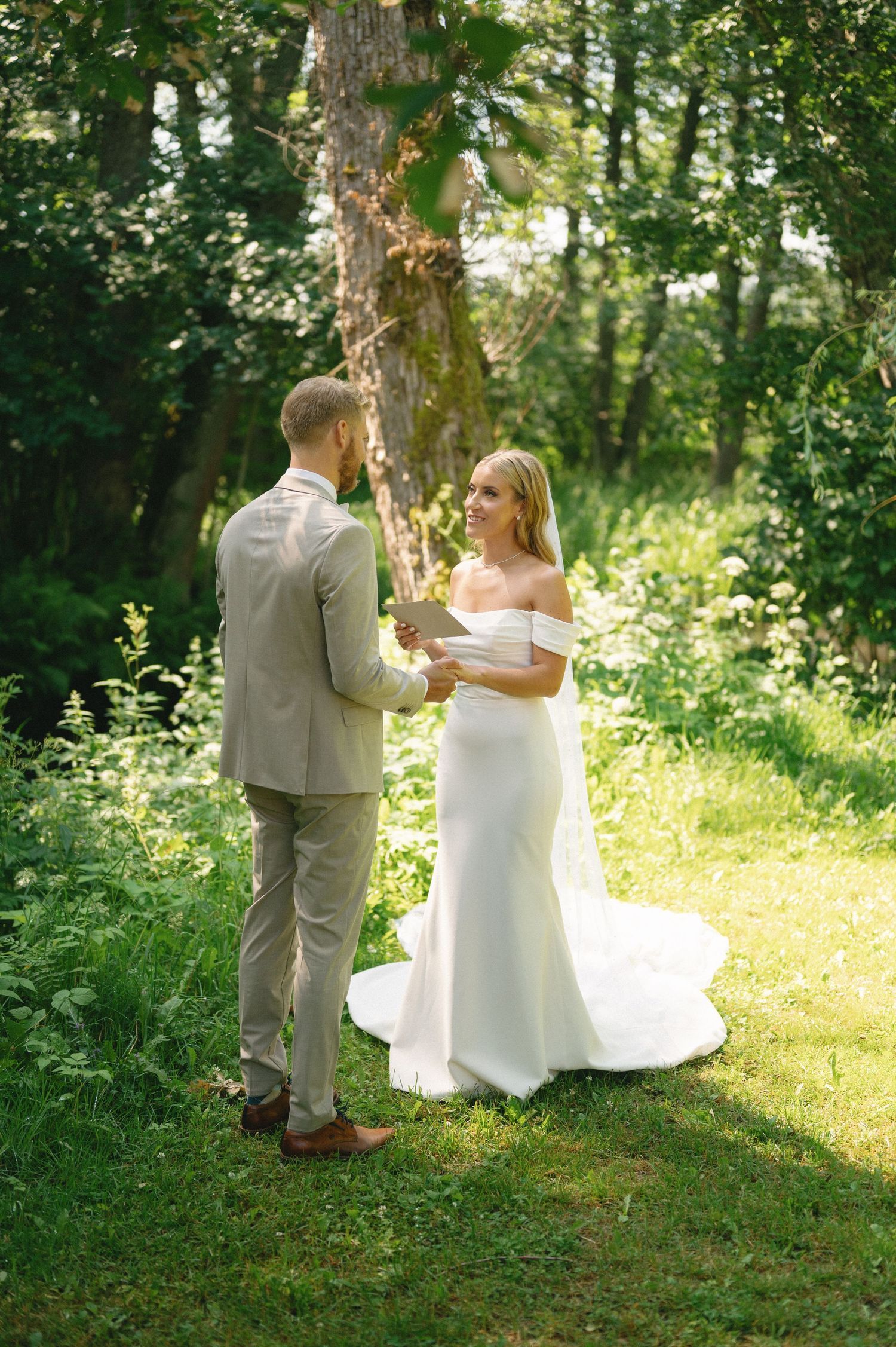 A couple shares an emotional moment while reading personal vows in a lush green forest setting.