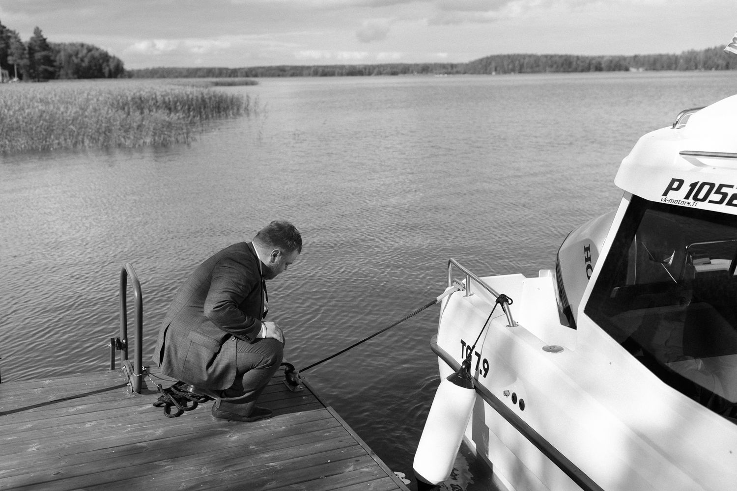 Group boarding boat at wooden dock with reeds and lake in background.